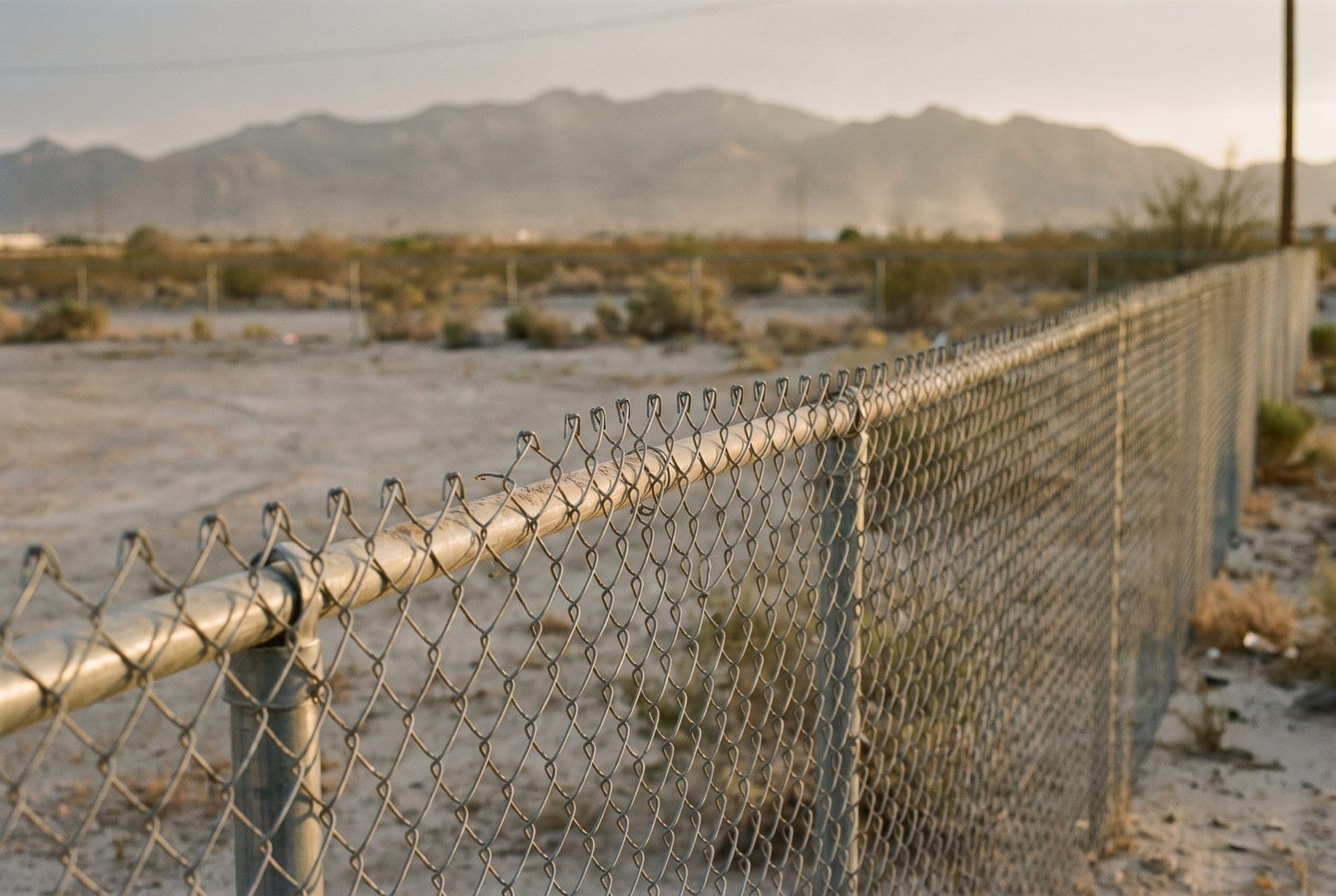 Galvanized commercial chain-link fence line at an El Paso commercial lot, low desert sun